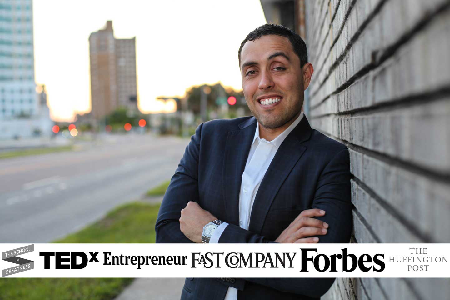 Jairek Robbins, founder of Performance Coach University, leaning against a brick wall on a city street