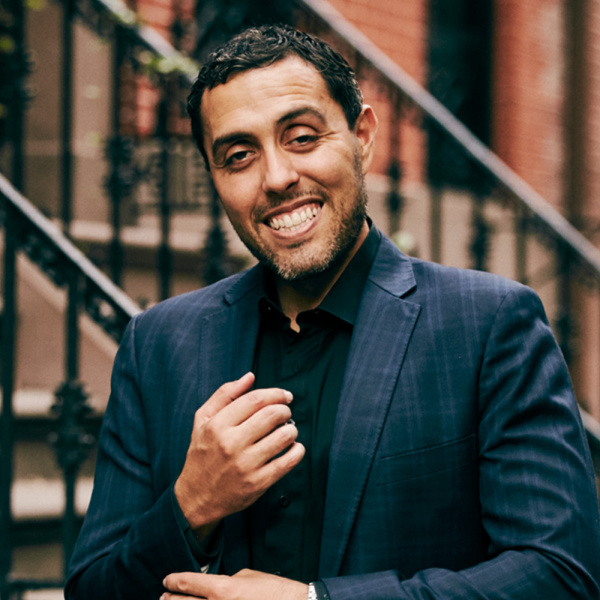 Jairek Robbins in a navy suit, seated on urban steps