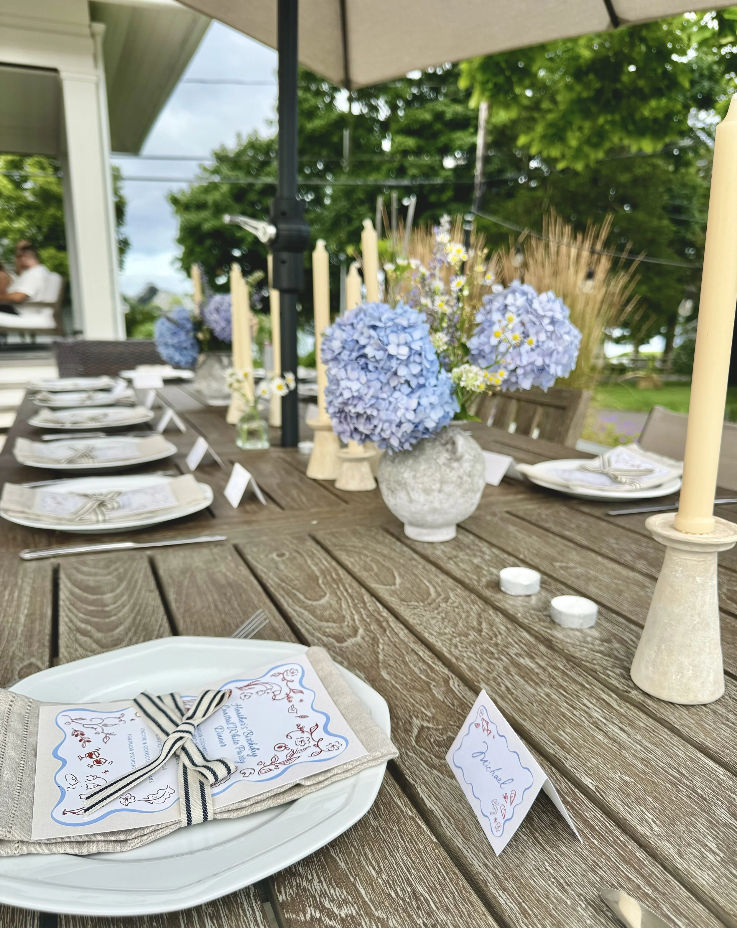 Outdoor patio table with blue hydrangeas, taper candles, linen napkins and illustrated menus