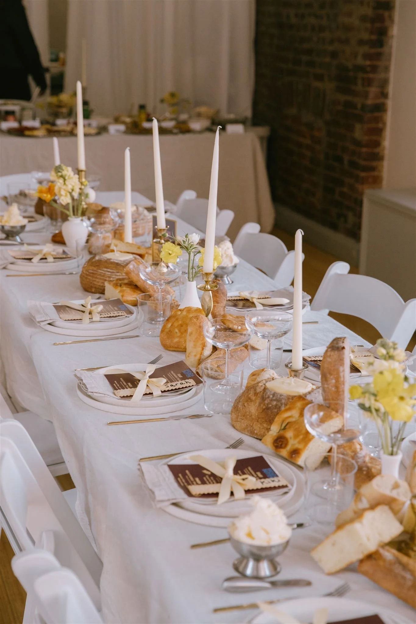 Long white-linen table set with artisan breads, taper candles, yellow flowers and place cards at a Bread & Butter Law event