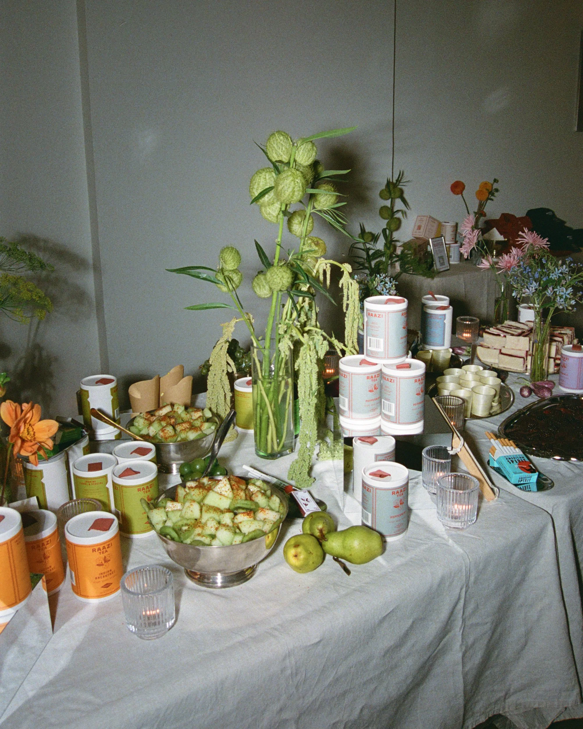 Raazi Tea display table with tea canisters, cucumber salad, pears and flowers