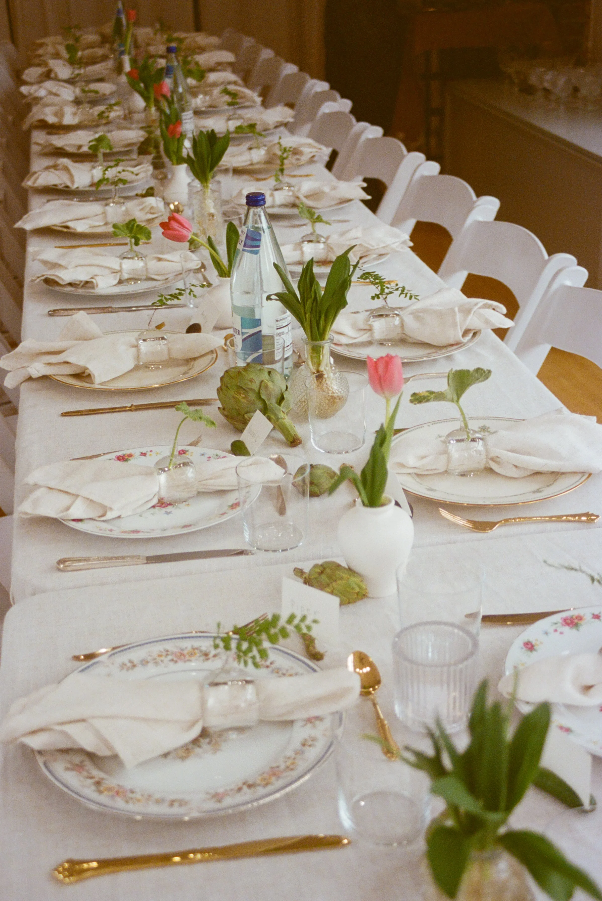 Overhead spring table with floral china, tulips in bud vases, artichokes and gold cutlery