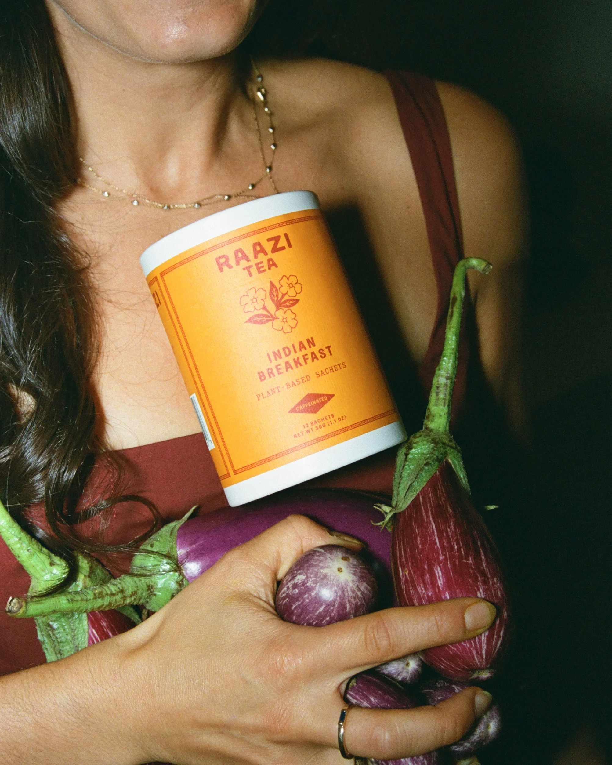 Woman holding a Raazi Tea Indian Breakfast canister and eggplants