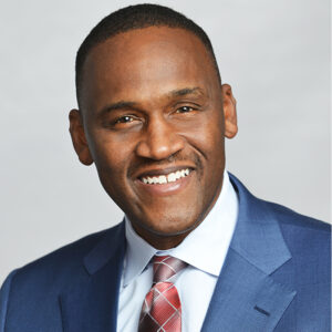 Darrell Andrews, smiling in a blue suit with a red plaid tie