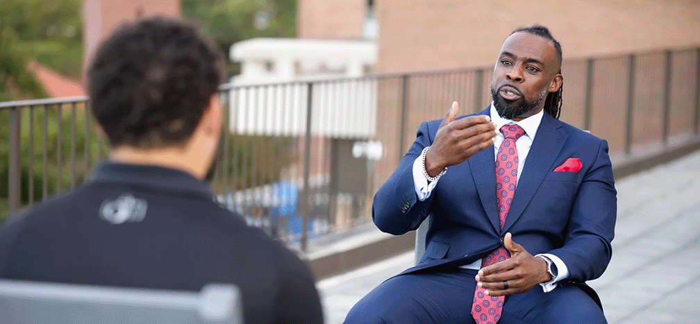 Leadership coaching session — a man in a navy suit speaking with another person on outdoor steps