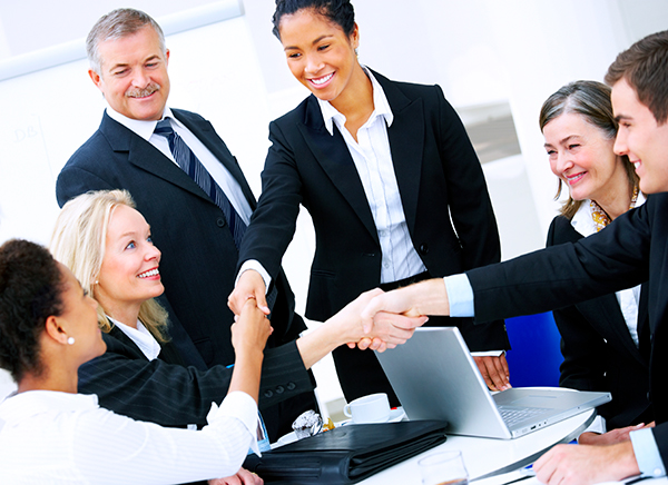 Group of smiling business professionals shaking hands around a conference table