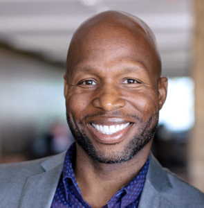 Mondoe Davis, smiling in a gray blazer and blue patterned shirt