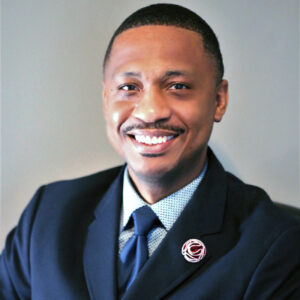 Jamoul, smiling in a dark suit with a lapel pin