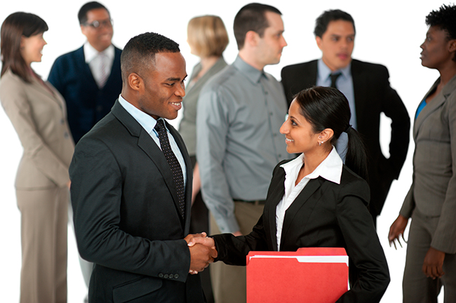 Two business professionals shaking hands with colleagues behind them