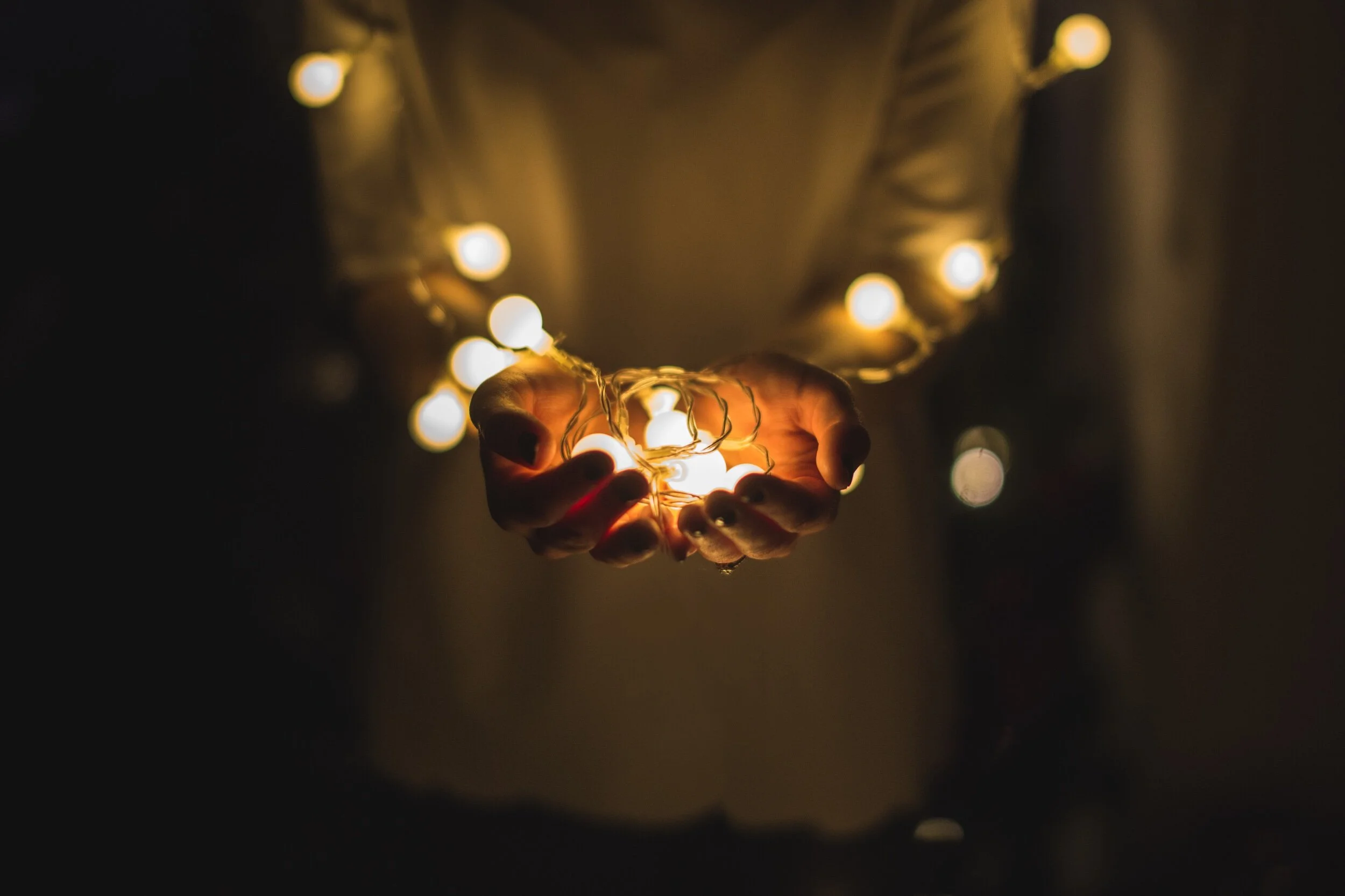 Hands cupping a glowing string of fairy lights against a dark background