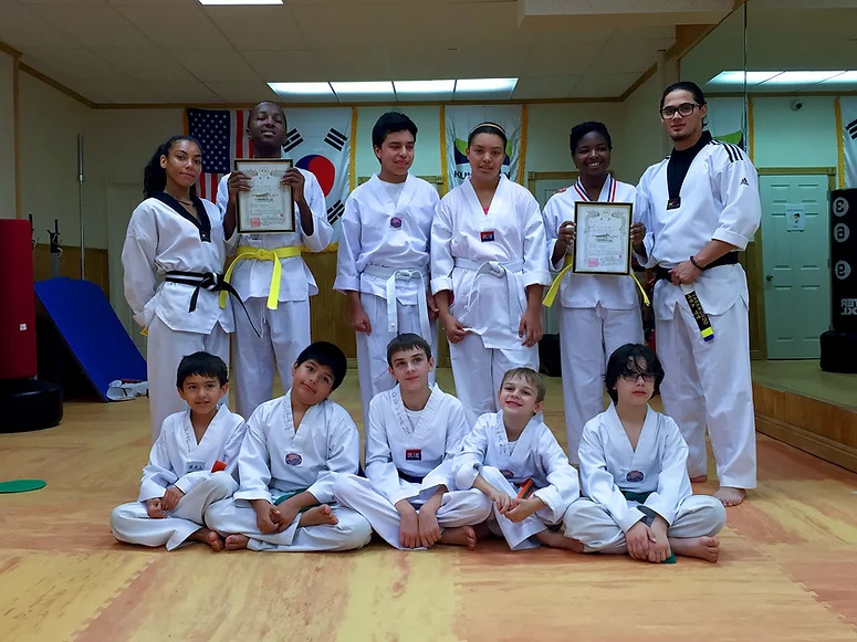 Group of children and adults in taekwondo uniforms posing in a martial arts studio