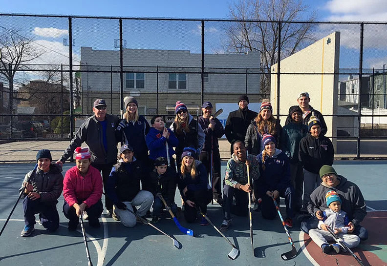 Large group of children and adults with street hockey sticks on an outdoor court
