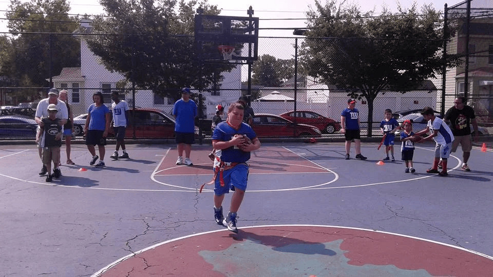 Children and adults playing flag football on an outdoor basketball court