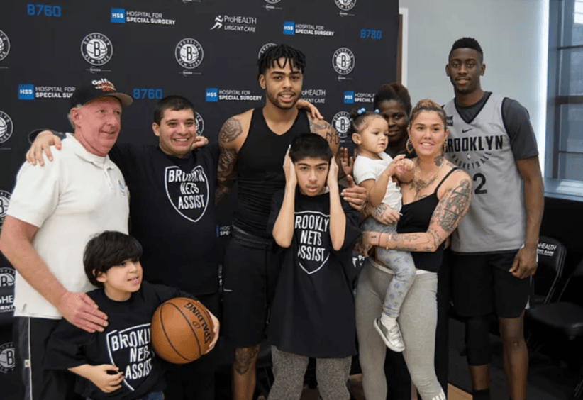 Group photo with Brooklyn Nets players and children wearing Brooklyn Nets Assist shirts at a sponsor backdrop