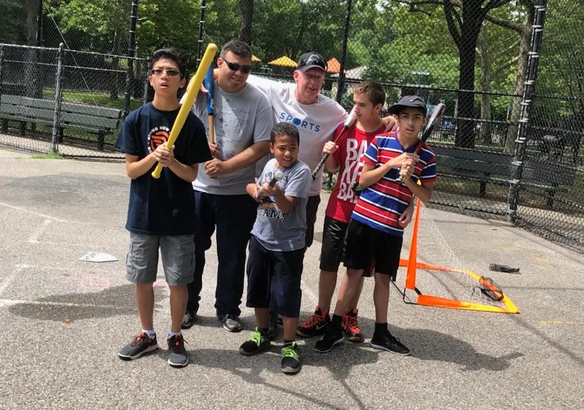Group of children and adults posing with toy baseball bats on an outdoor court