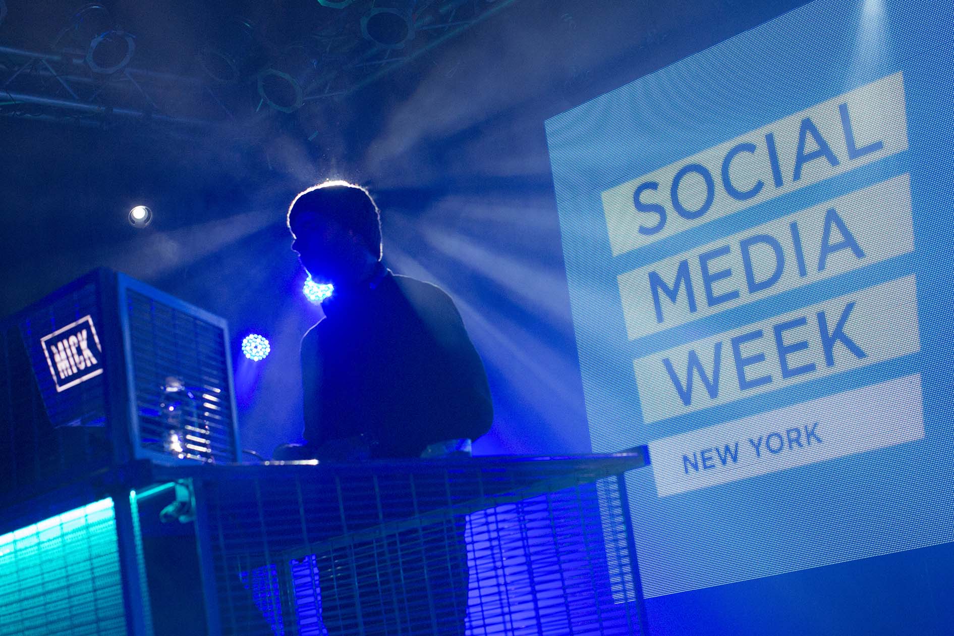 DJ silhouetted in blue stage lighting at Social Media Week New York, with a large LED screen behind