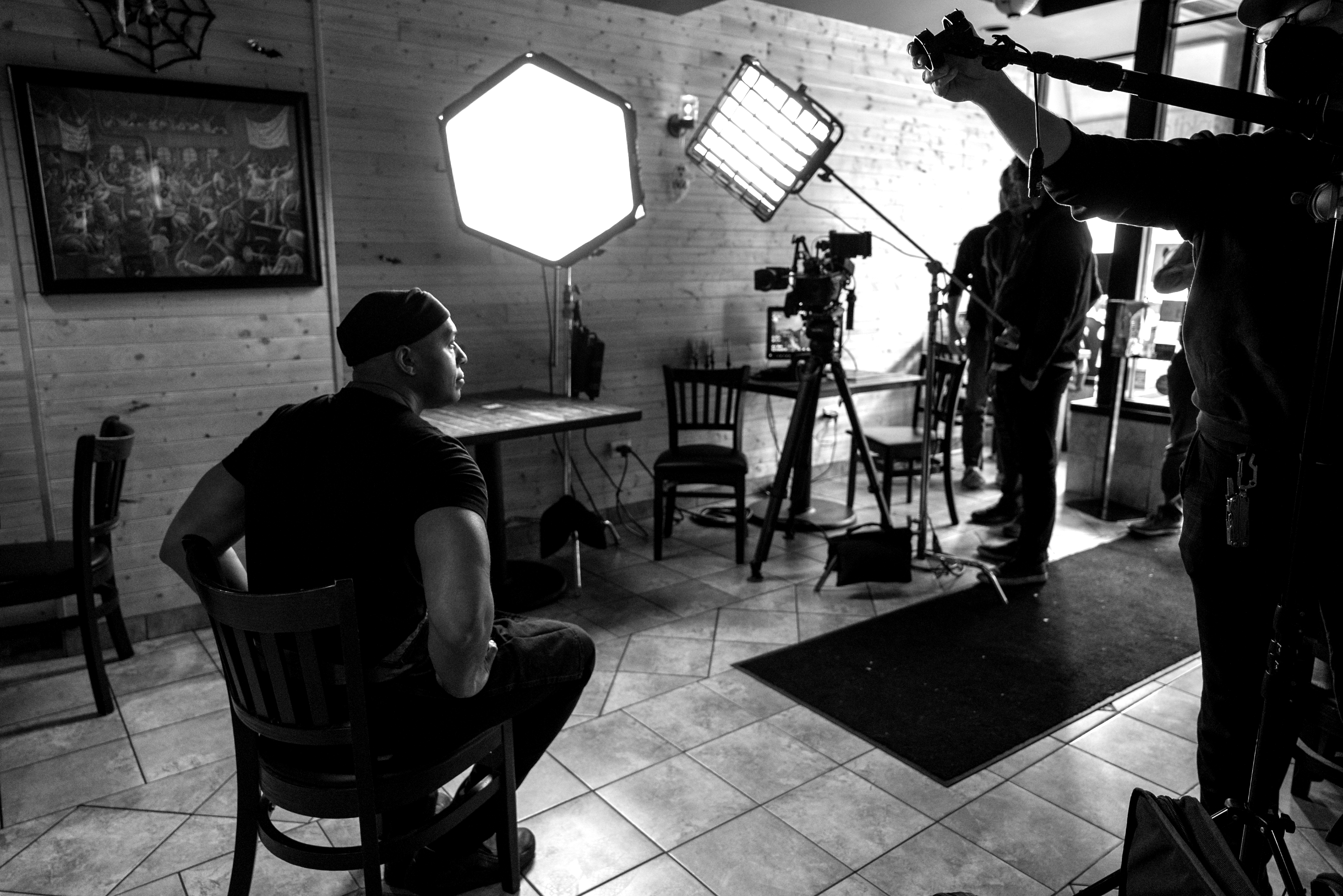 Black-and-white behind-the-scenes shot: a subject filmed with a professional camera and lighting rig