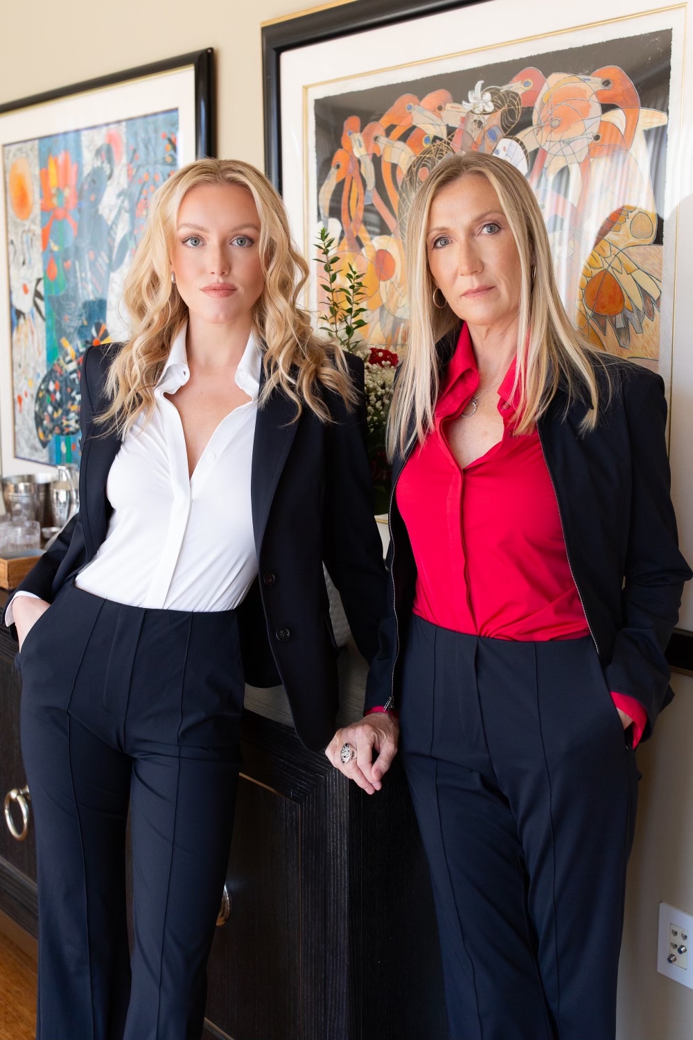 Two women in matching black power suits standing in front of colourful abstract artwork — the Possible team