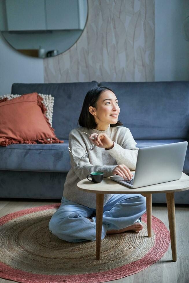 Woman sitting cross-legged on the floor working on a laptop at a low table in a cosy living room