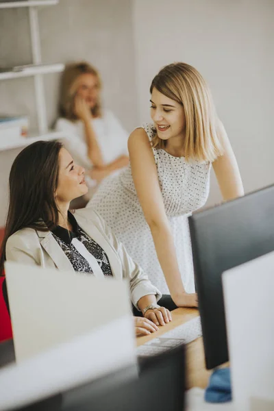 Two businesswomen at a desk looking at a computer monitor and smiling