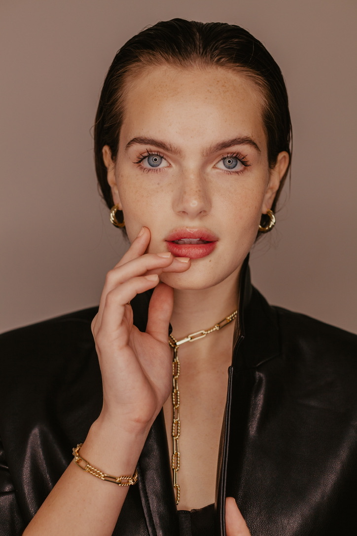 Dark-haired woman in gold hoop earrings, chain and bracelet with a black leather jacket