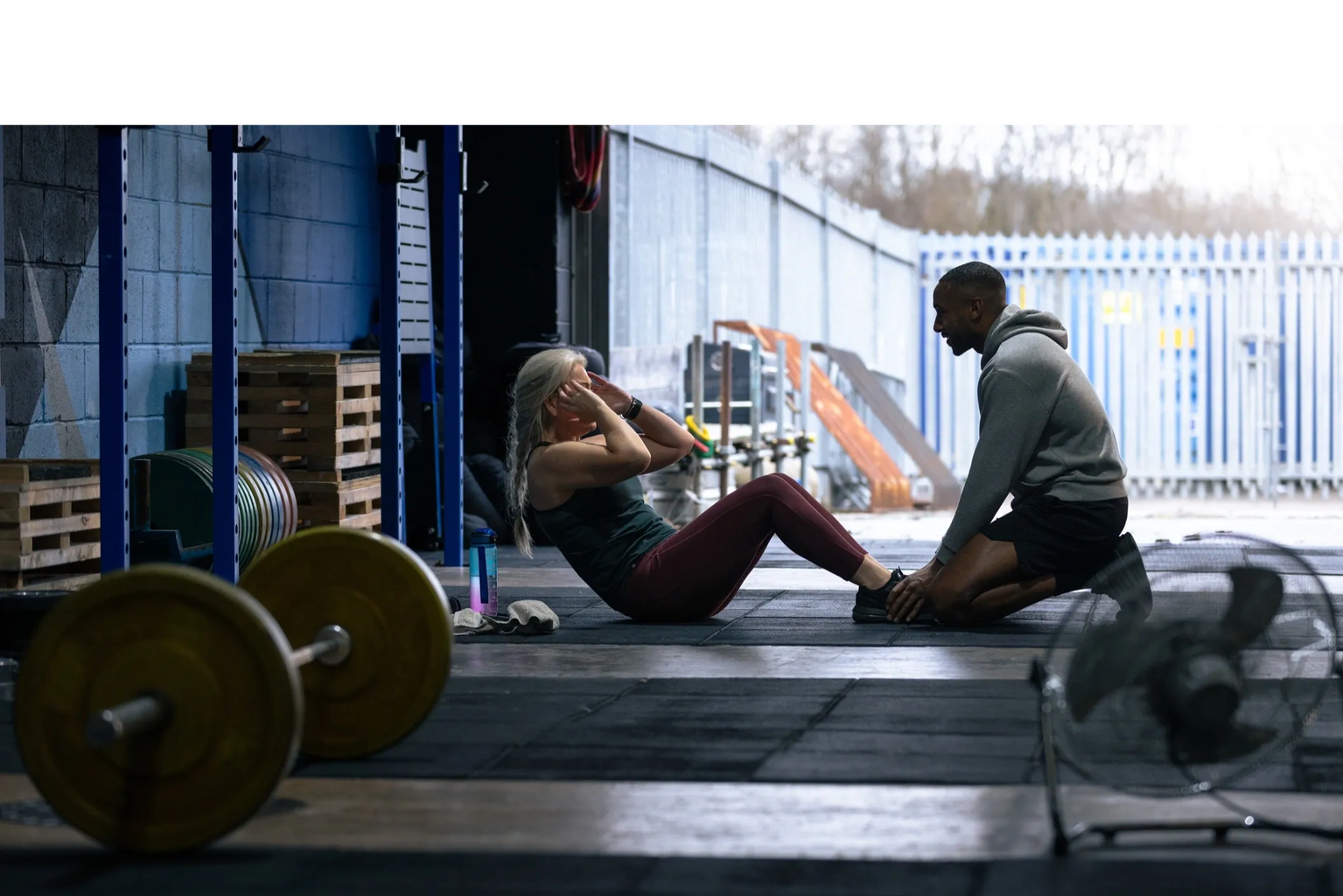 Female client doing sit-ups assisted by a male personal trainer in an industrial gym