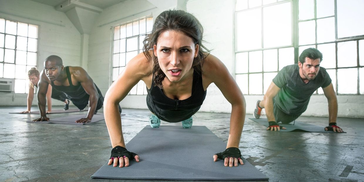 Group fitness class doing push-ups on yoga mats in a bright industrial studio