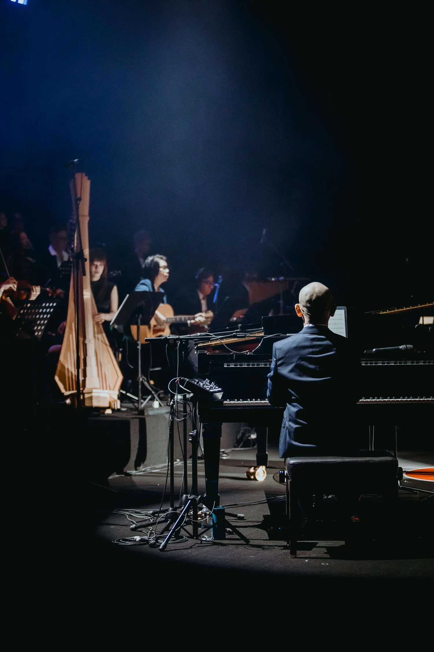 Pianist performing with an orchestra ensemble under a dramatic blue stage spotlight.
