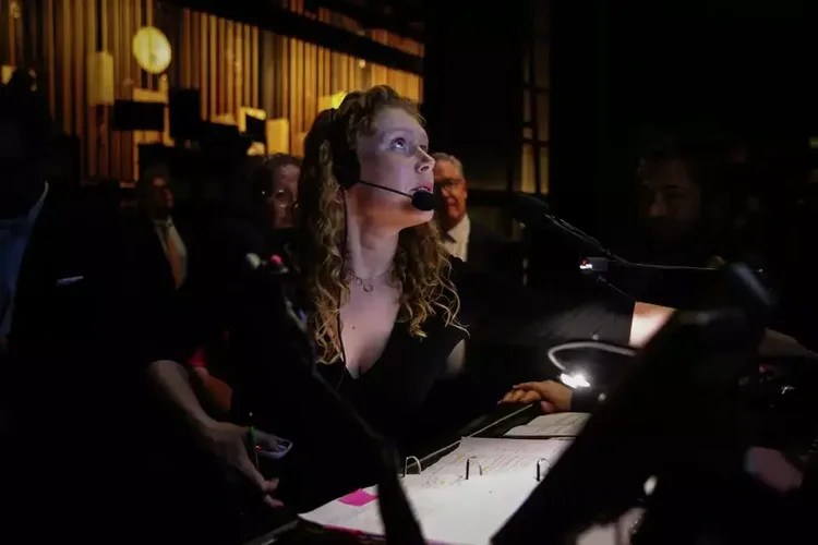 Jayme O'Hara wearing a headset backstage at a music event, looking up toward the stage.