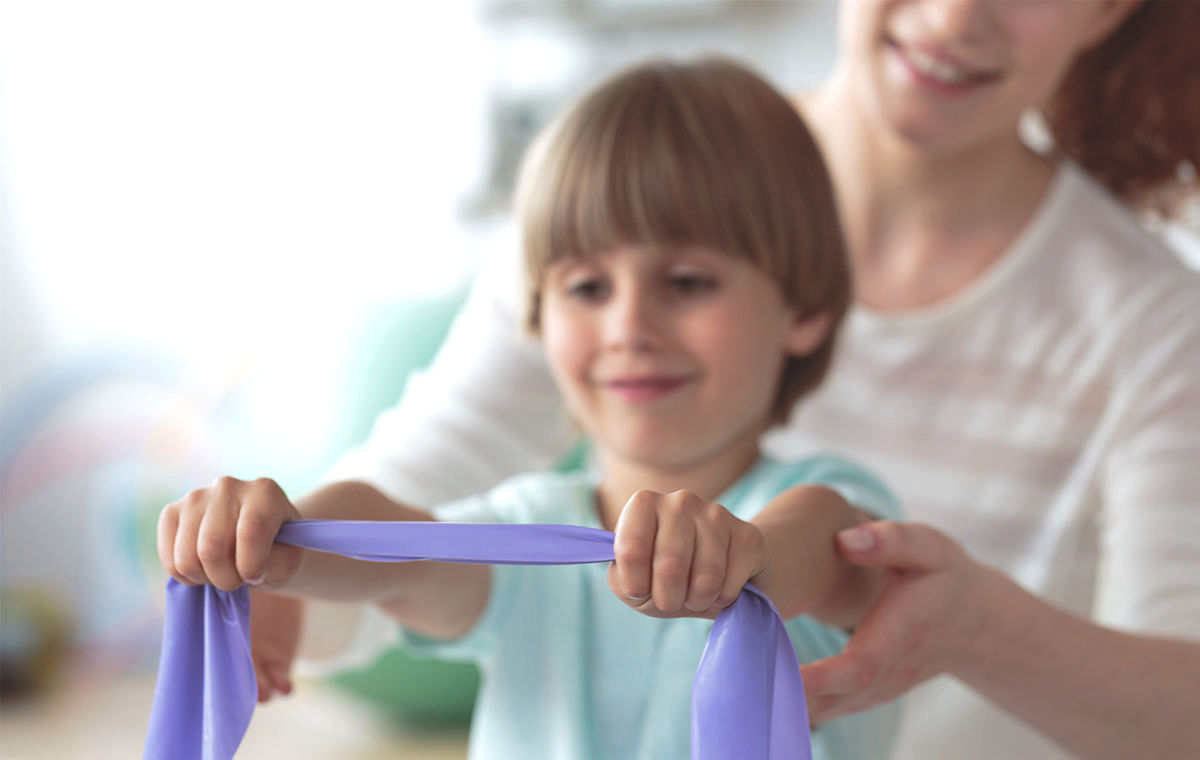 Child and therapist using a resistance band during a pediatric physical therapy session