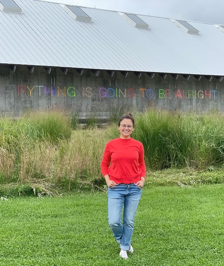 Dr. Ruxandra Bogaciu in a red sweater in front of an 'Everything Is Going To Be Alright' barn