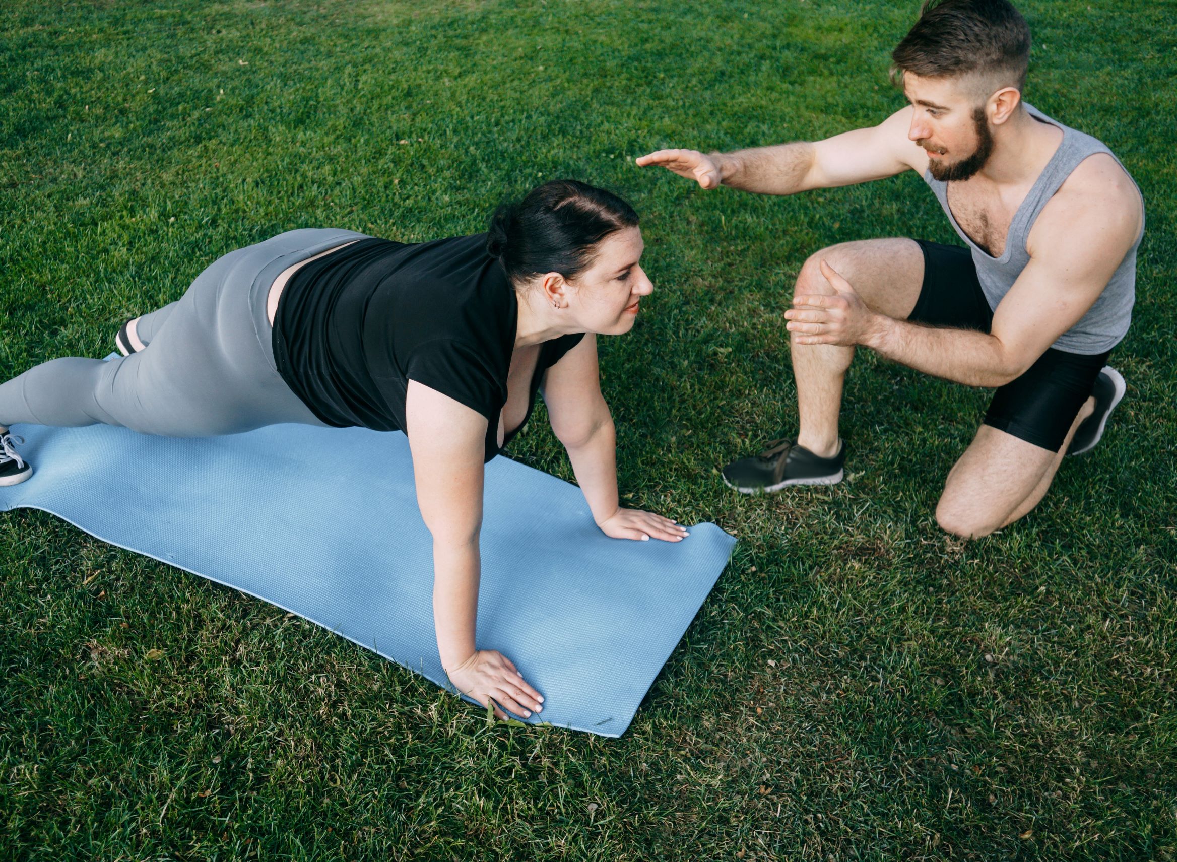 Trainer coaching a woman through a plank on a mat outdoors
