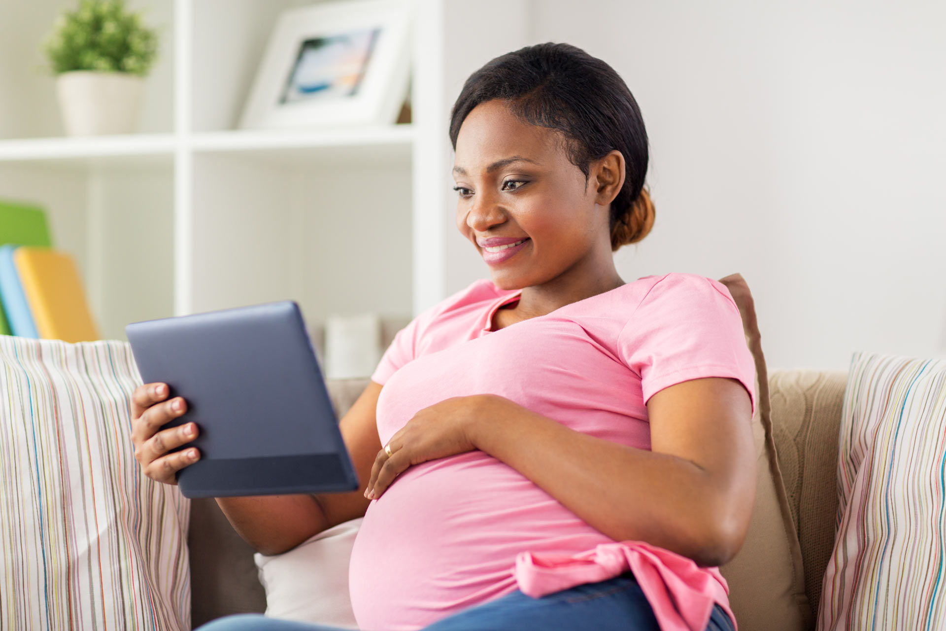 Pregnant woman smiling at a tablet on her couch