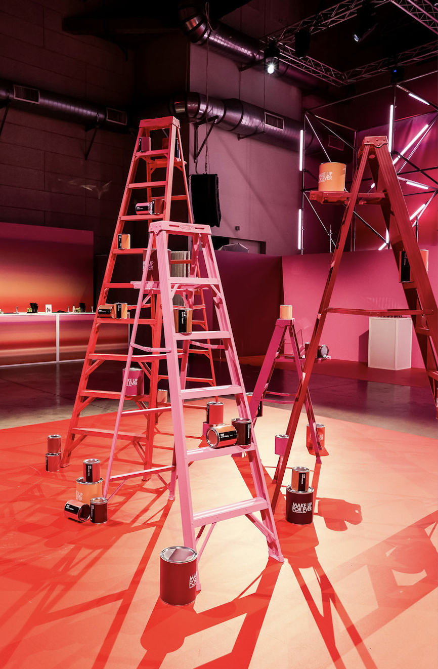 Pink and red painted ladders with Make Up For Ever branded paint cans in an event space