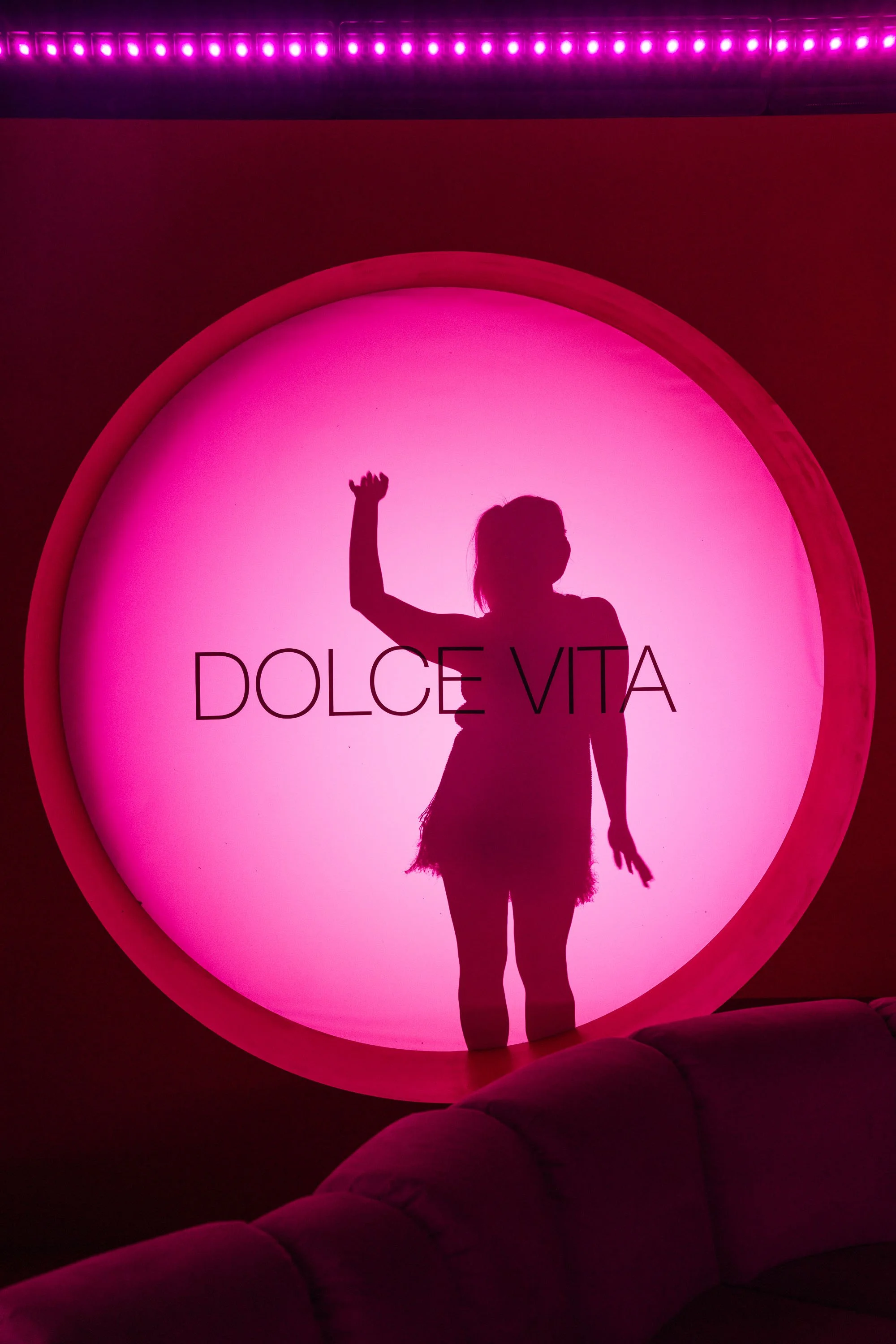 Silhouette against a magenta circular Dolce Vita neon light installation