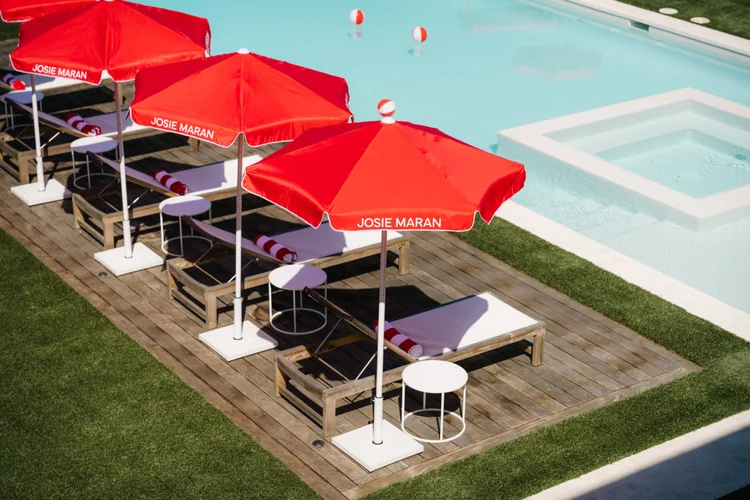 Red Josie Maran branded beach umbrellas beside a pool