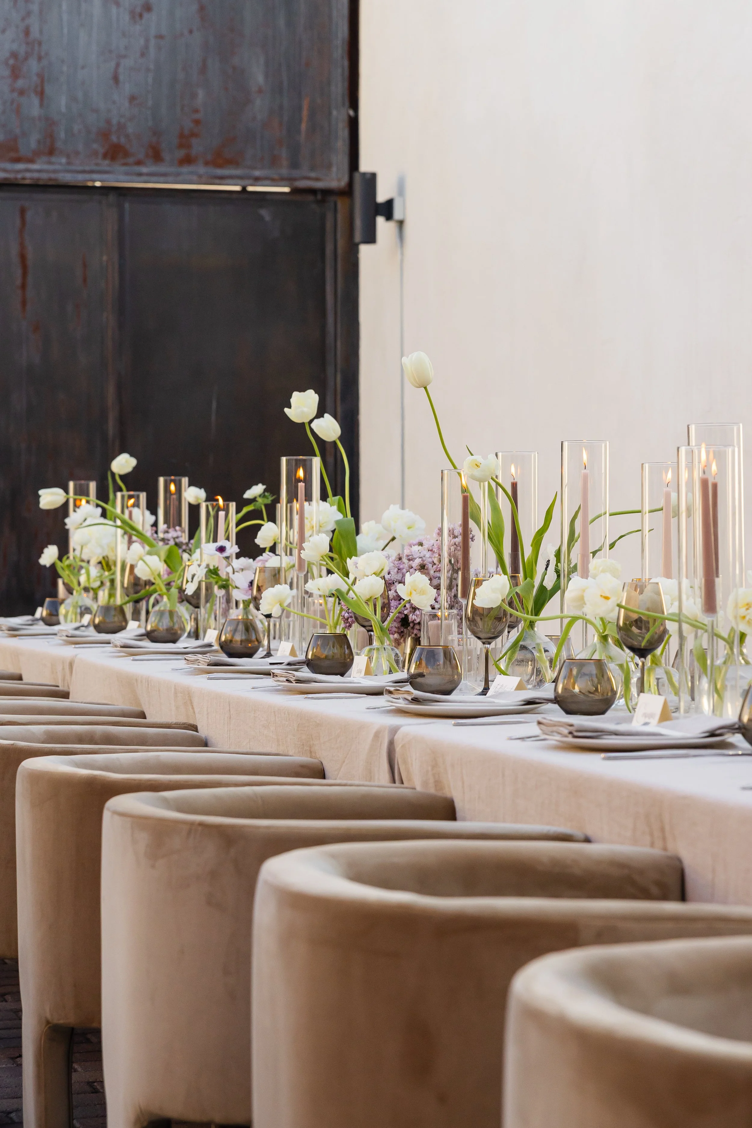 Elegant long dining table set with white tulip florals, tapered candles and velvet chairs for a Bobbi Brown dinner