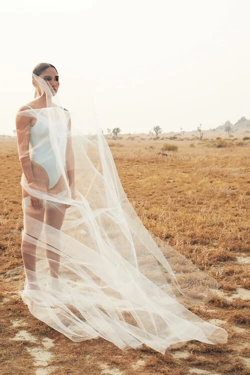 Model in a white bodysuit with a billowing tulle veil in the desert for SKIMS Bridal