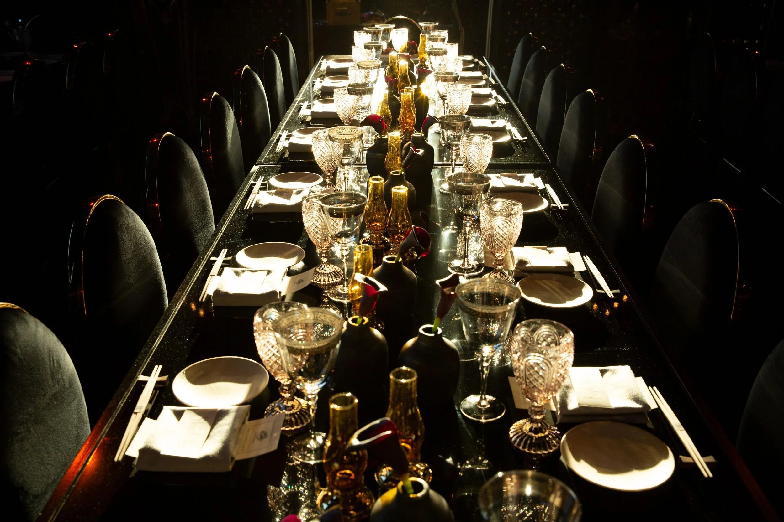 Dark, dramatically lit long dinner table set with crystal glassware for the François Nars birthday event