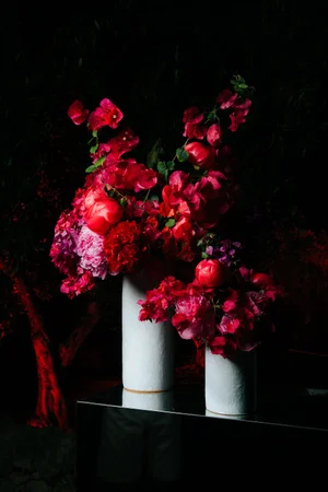 Red bougainvillea floral arrangement in white vases against a dark backdrop