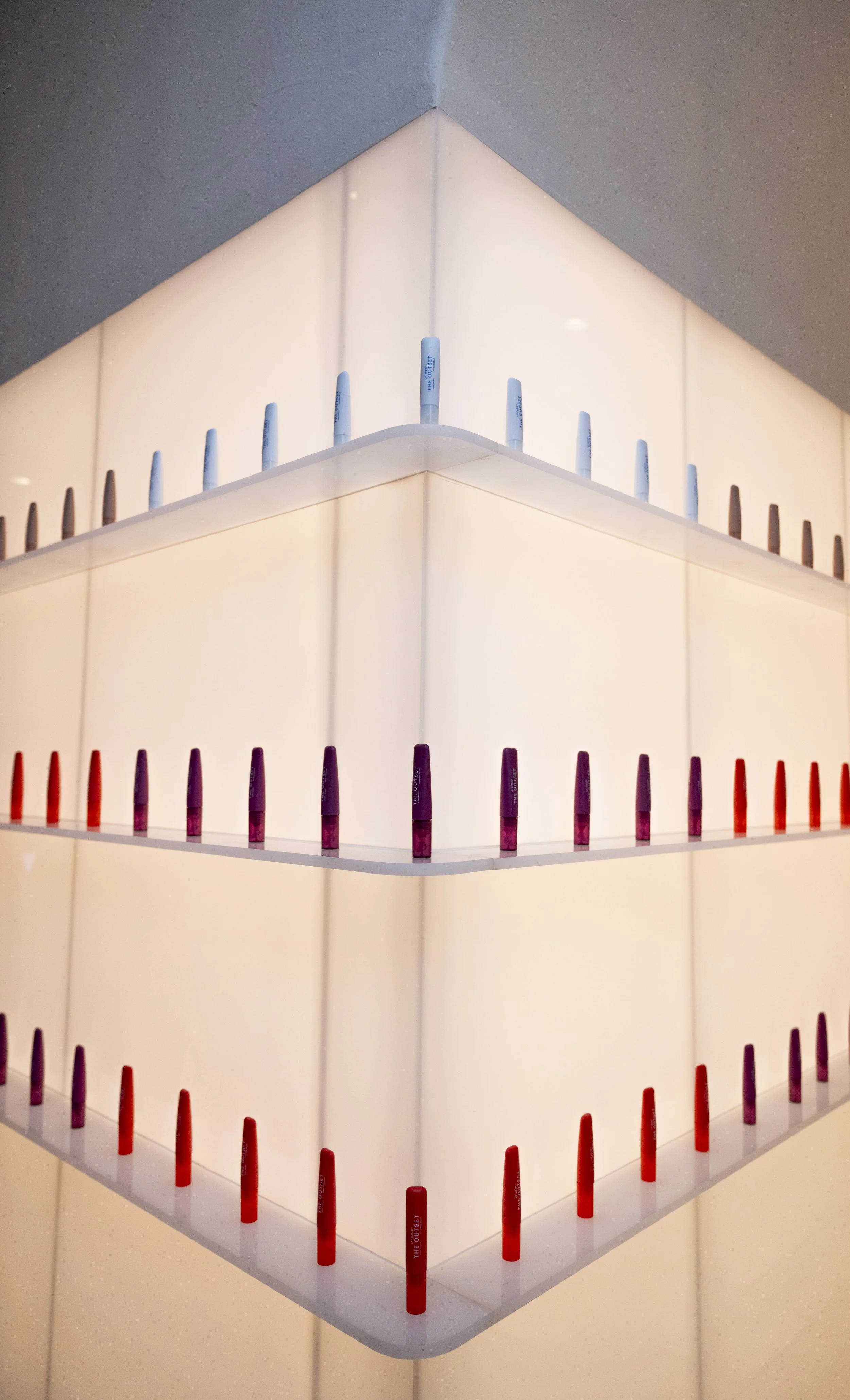 Illuminated corner shelving lined with rows of colorful lip sticks for The Outset Lip Oasis