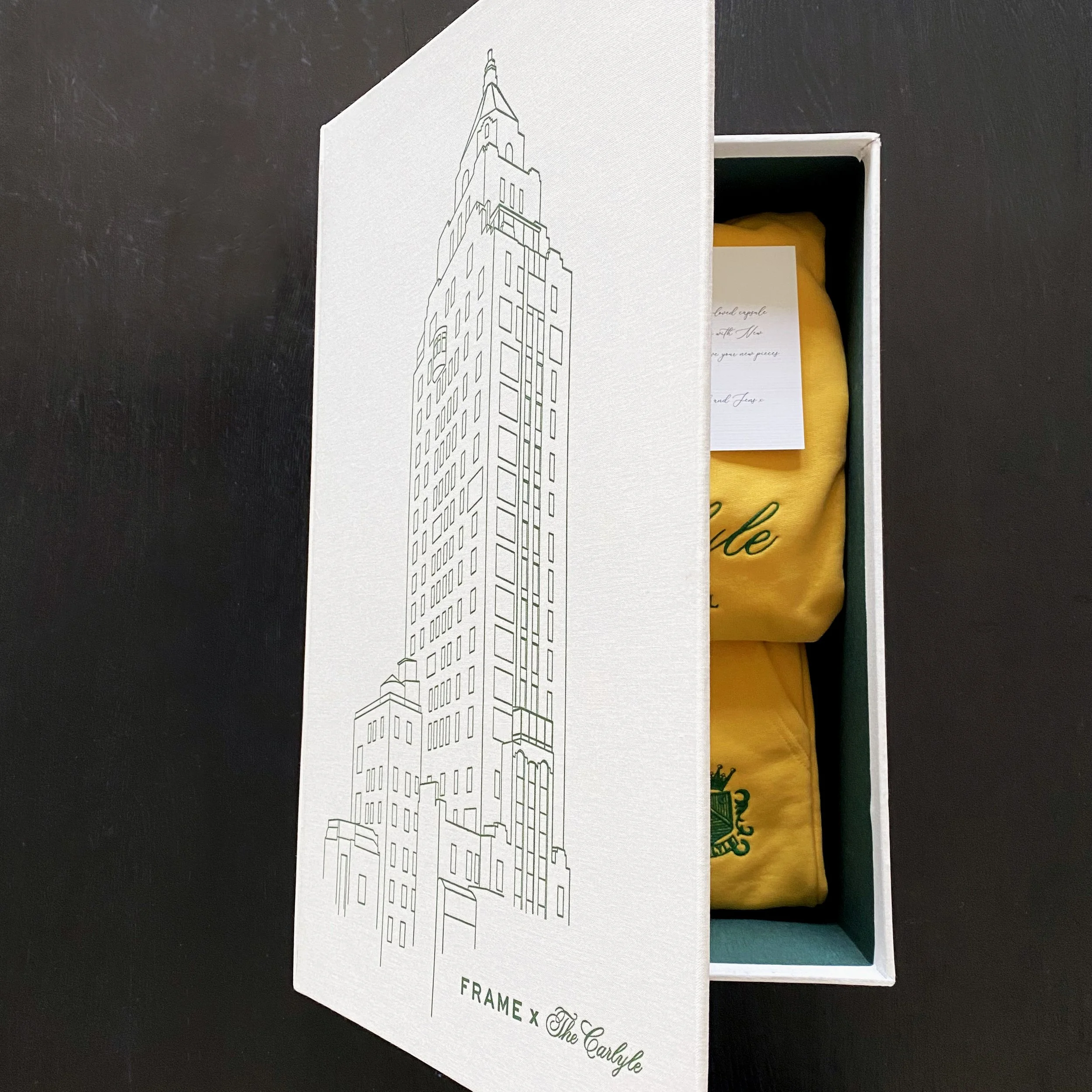 Frame x The Carlyle gift box open to reveal a yellow sweatshirt with a printed card