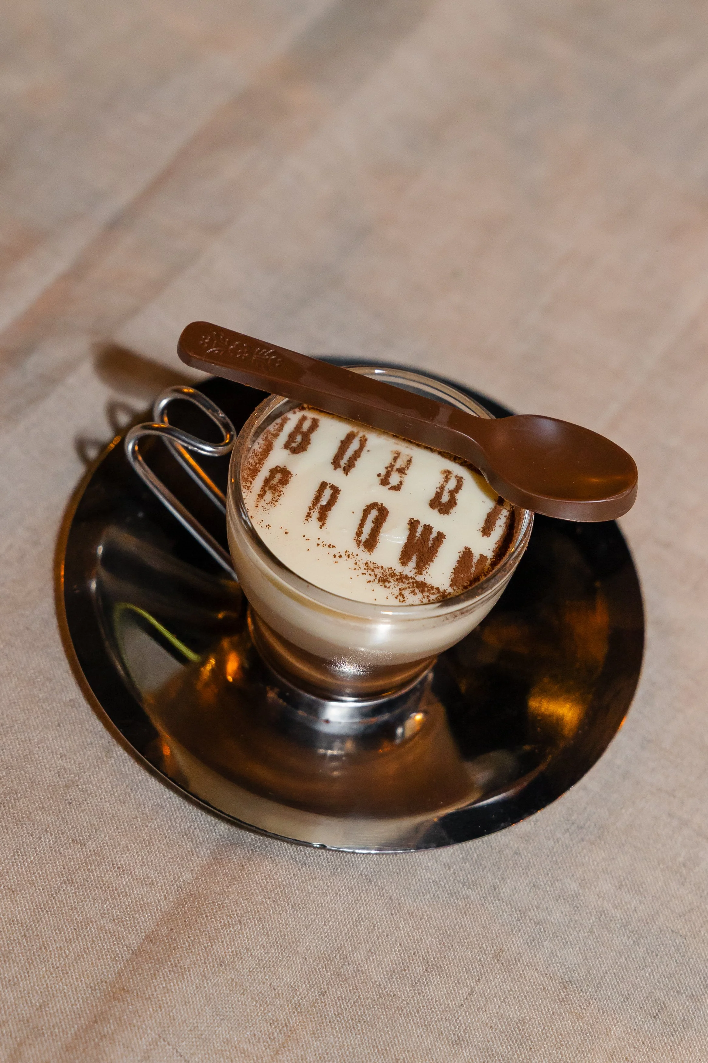 Bobbi Brown branded latte art dessert in a glass cup on a silver saucer
