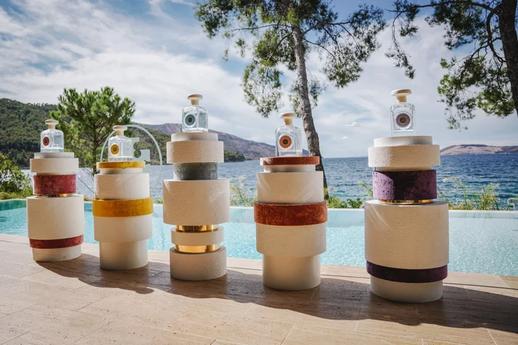 Tory Burch Essence of Dreams fragrance bottles on sculptural pedestals by a pool