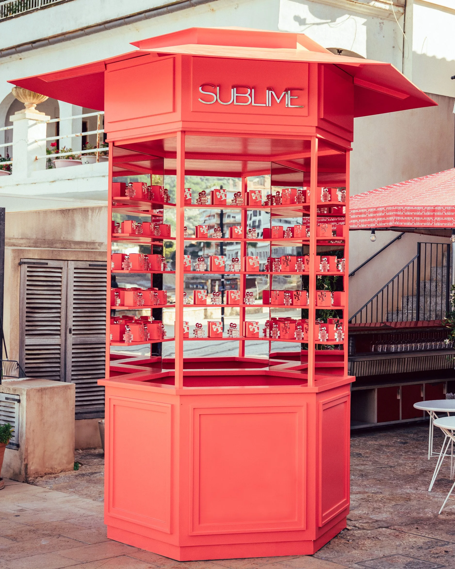 Coral-red octagonal outdoor kiosk branded SUBLIME stocked with red product gift boxes