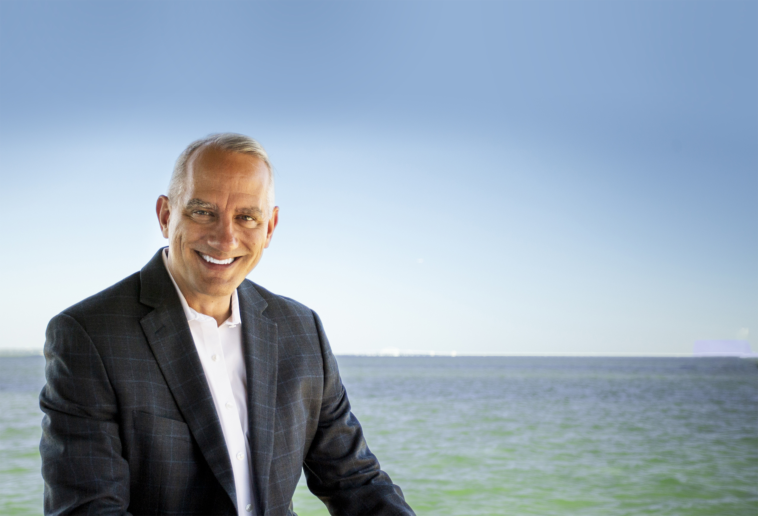 Joe Mikalajunas, executive coach, in a dark blazer smiling outdoors by the ocean in Tampa Bay
