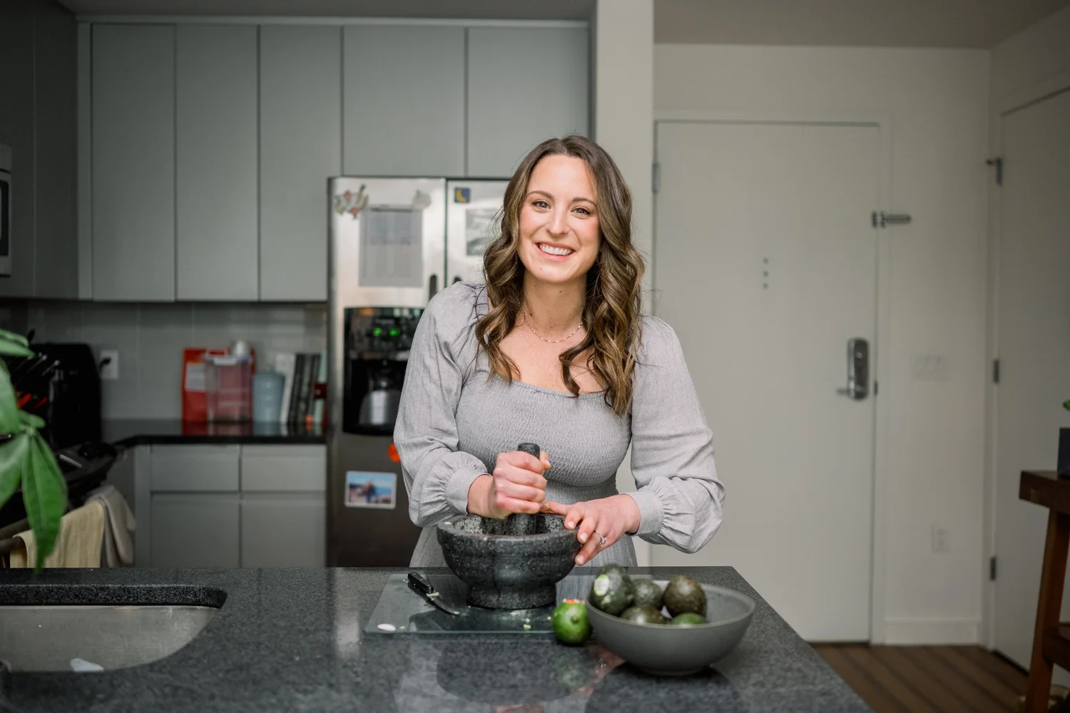 Rachel Naar in her kitchen preparing food with a mortar and pestle, a bowl of avocados beside her