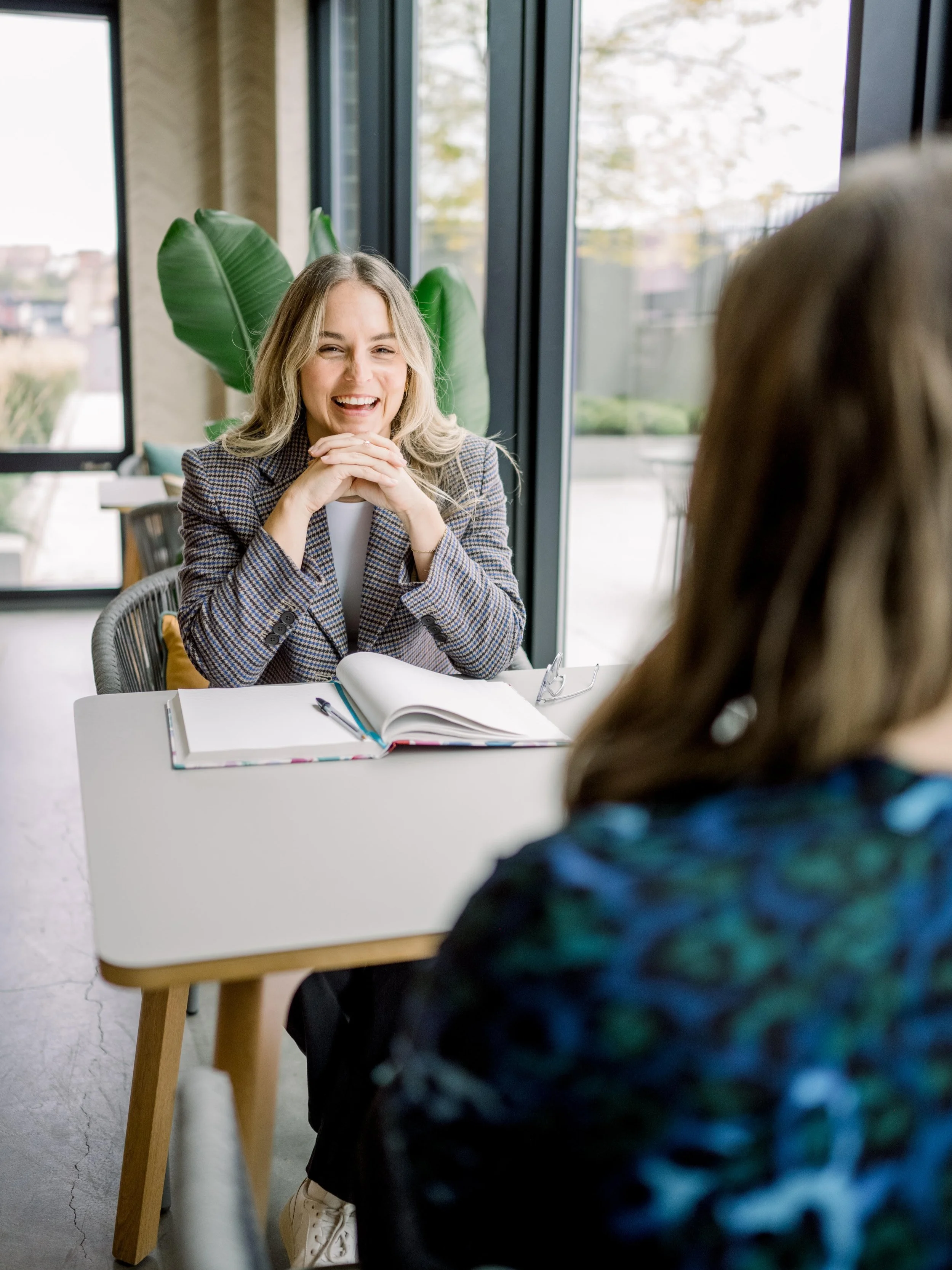 Rachel Naar in a bright office seated across a table from a client with an open notebook, both laughing