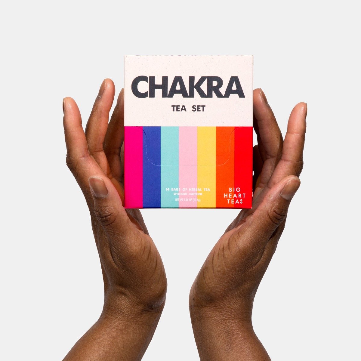 Two hands holding a colorful Chakra Tea Set box by Big Heart Teas