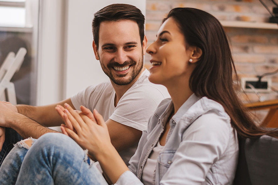 Smiling couple sitting closely together on a couch, holding hands and laughing